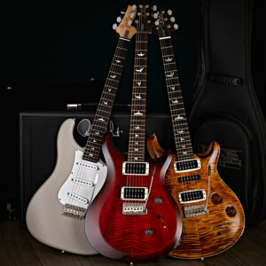 Three PRS guitars stood up against an amp